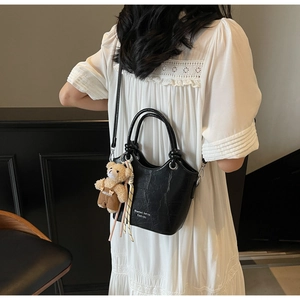 Detail of black crocodile texture leather bag with plush bear charm and striped ribbon