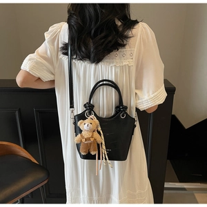Detail of black crocodile texture tote bag with a cute teddy bear charm accessory