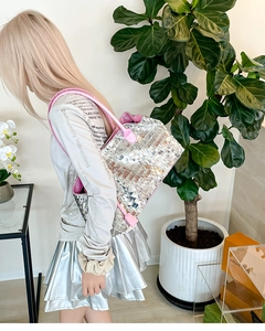 Detail of silver sequin tote bag with pink leather strap held by a model in a room