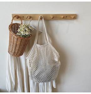 Detail of cream cotton mesh shopping bag with long handles hanging on a wooden hook