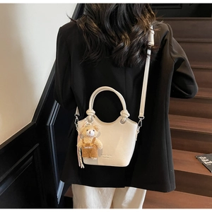 Detail view of white crocodile pattern bucket bag with teddy bear charm on model
