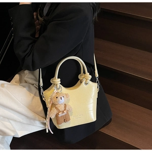 Detail of yellow crocodile embossed bucket bag featuring a cute plush bear pendant accessory