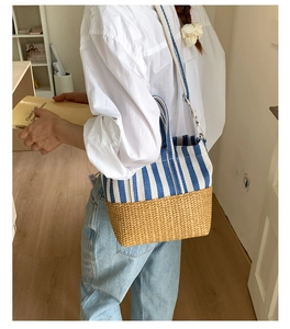 Detail of blue and white striped canvas tote bag with woven straw bottom on model