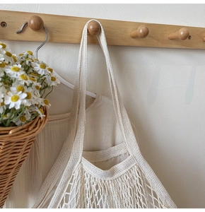 Detail of a large woven cotton mesh shopping bag with inner lining hanging on a wooden hook