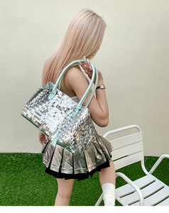 Detail of silver sequin tote bag with mint green leather handles and reflective texture