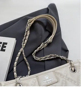 Détail d'un sac bandoulière beige matelassé sur veste grise avec focus sur la bandoulière