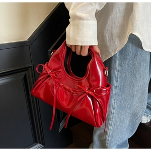 Detail of red patent leather handbag with bow accents held by a person in white shirt