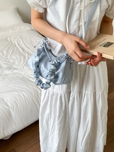 Sac nuage plissé bleu clair au fini brillant, porté en bandoulière pour un look chic
