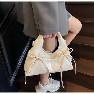 Detail of cream glossy leather handbag with bow accents on a stylish wooden staircase