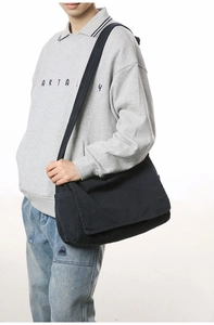 Detailed view of the black canvas messenger bag worn across the body by a model
