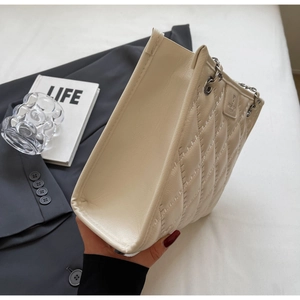Détail du sac bandoulière beige matelassé avec chaîne argentée et patch de marque gaufré