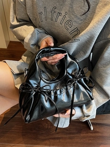 Glossy black dumpling bag with bow details and ruched texture in a stylish handheld pose