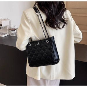 Détail d'un sac bandoulière matelassé noir avec chaîne en métal et logo argenté élégant
