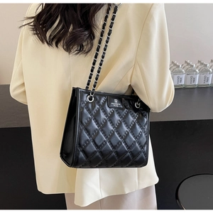 Détail du sac cabas matelassé noir avec bandoulière chaîne argentée porté par un mannequin