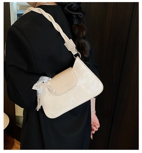 Detail of cream patent leather underarm bag with woven strap and lace ribbon charm