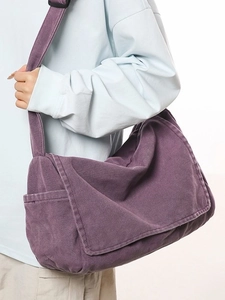 Large purple washed canvas messenger bag with wide strap worn by a model in studio