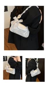 Detail of silver metallic handbag with woven strap and white lace bow decoration