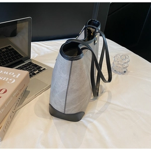 Large grey tote bag with black trim placed by a laptop in a minimalist lifestyle setting