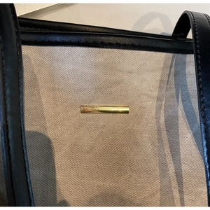 Detail of canvas texture, black leather strap, and gold metal hardware on the tote bag