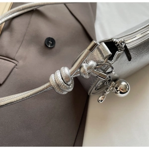 Detail of silver pleated shoulder bag featuring knotted strap and metallic spherical charm