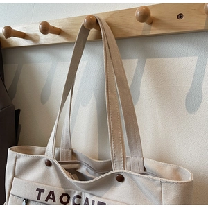 Detail of beige canvas tote bag with brown TAOCAI print on a wooden wall hanger