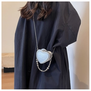 Macro shot of silver heart-shaped mini crossbody bag with embossed text and metal chain