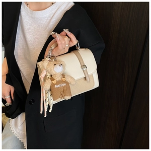 Detail of beige woven crossbody bag with cute teddy bear charm and metal buckle