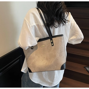 Detail of large beige tote bag with black contrast trim and golden logo plate