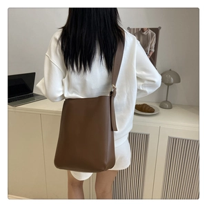 Brown leather bucket bag with wide adjustable shoulder strap shown on model in a cozy setting