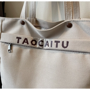 Close-up of canvas tote bag showing zipper detail, brown buttons and brand lettering