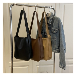Three minimalist leather hobo bags in black, dark brown, and beige hanging on rack