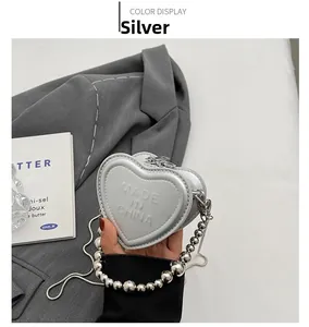 Macro detail of silver heart-shaped mini crossbody bag with embossed lettering and metal chain