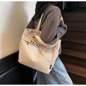 Detail of beige canvas tote bag showing side pockets and zipper compartment on shoulder