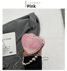 Detail of pink heart-shaped bag with silver bead chain and embossed logo on grey blazer