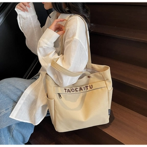 Close-up of beige canvas tote with zipper pocket, side pocket and letter embroidery