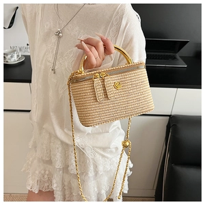 Detailed macro view of woven straw box bag with gold rose relief and chain strap