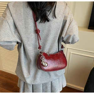 Close-up of a burgundy leather crescent bag with wrinkled texture and silver ball charm