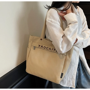 Khaki canvas tote bag with brand logo shown on a model in a casual lifestyle setting