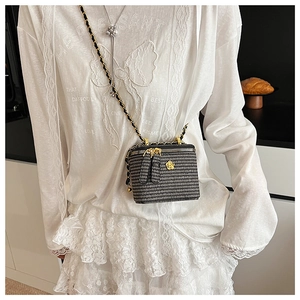 Detail of a woven textured crossbody bag with gold camellia floral clasp and chain strap
