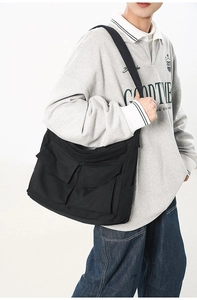 Détail du grand sac messager en toile noire avec poches plaquées pour un usage quotidien