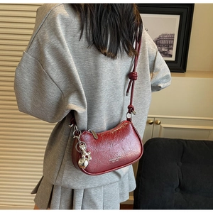 Detail of burgundy crescent shoulder bag with pleated texture and metallic charms