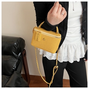 Detail of yellow knit handbag with golden camellia clasp and chain strap on person