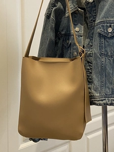 Minimalist khaki leather tote bag hanging on a rack with a denim jacket background