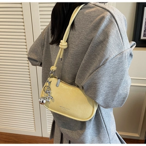 Detail of light yellow ruched underarm bag with knot strap and silver balloon dog charm