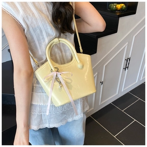 Detail of light yellow leather bucket bag with pink ribbon bow and pearl heart charm