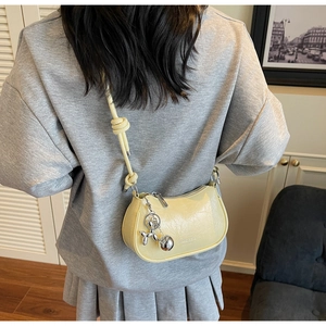 Detail of creamy yellow crescent bag with crinkled texture and silver balloon dog charm