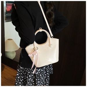 Detail of beige glossy crossbody bag featuring pink ribbon and pearl charm accessory