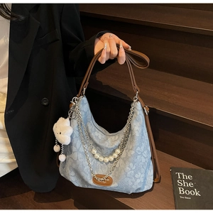 Close-up of denim tote bag featuring white pearl chain and metal strap detail