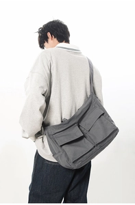 Détail du sac messager en toile gris foncé avec de grandes poches à rabat et sangle