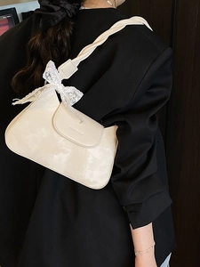 Cream white shoulder bag featuring a lace bow charm and unique twisted chain strap design